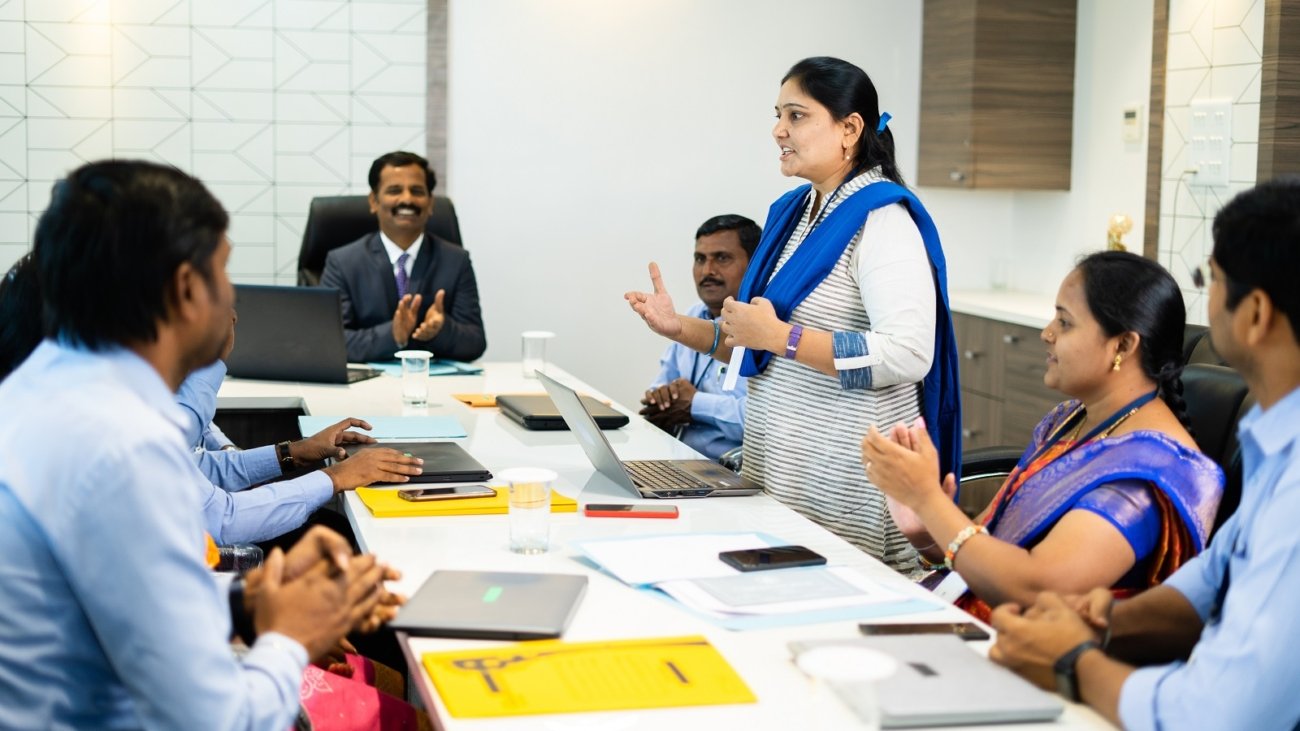 woman employee speaking confidently at board meeting in front of cowrkers - concept of briefing strategy, business planning and leadership.