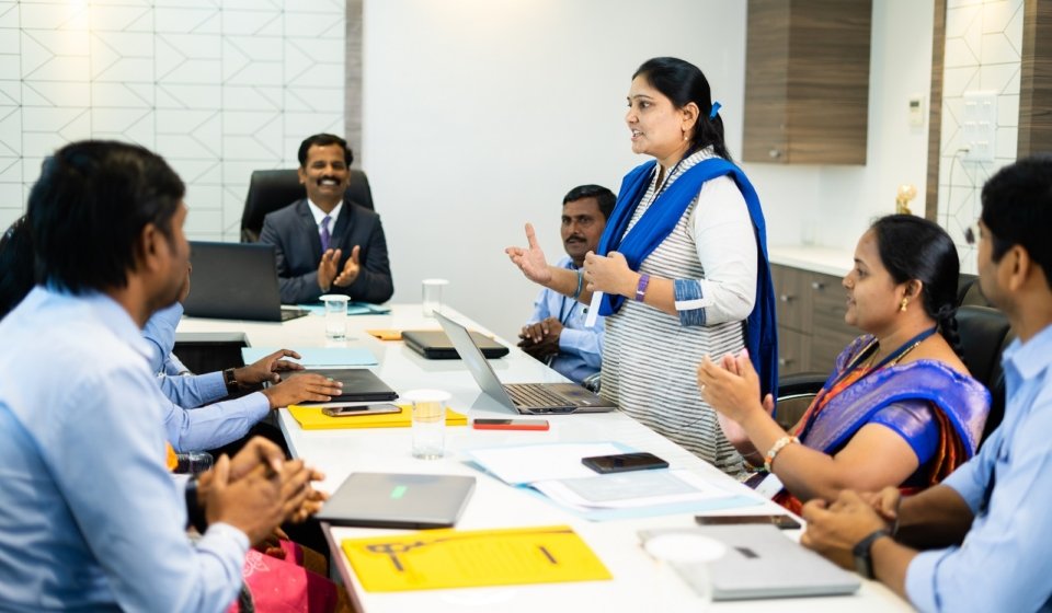 woman employee speaking confidently at board meeting in front of cowrkers - concept of briefing strategy, business planning and leadership.
